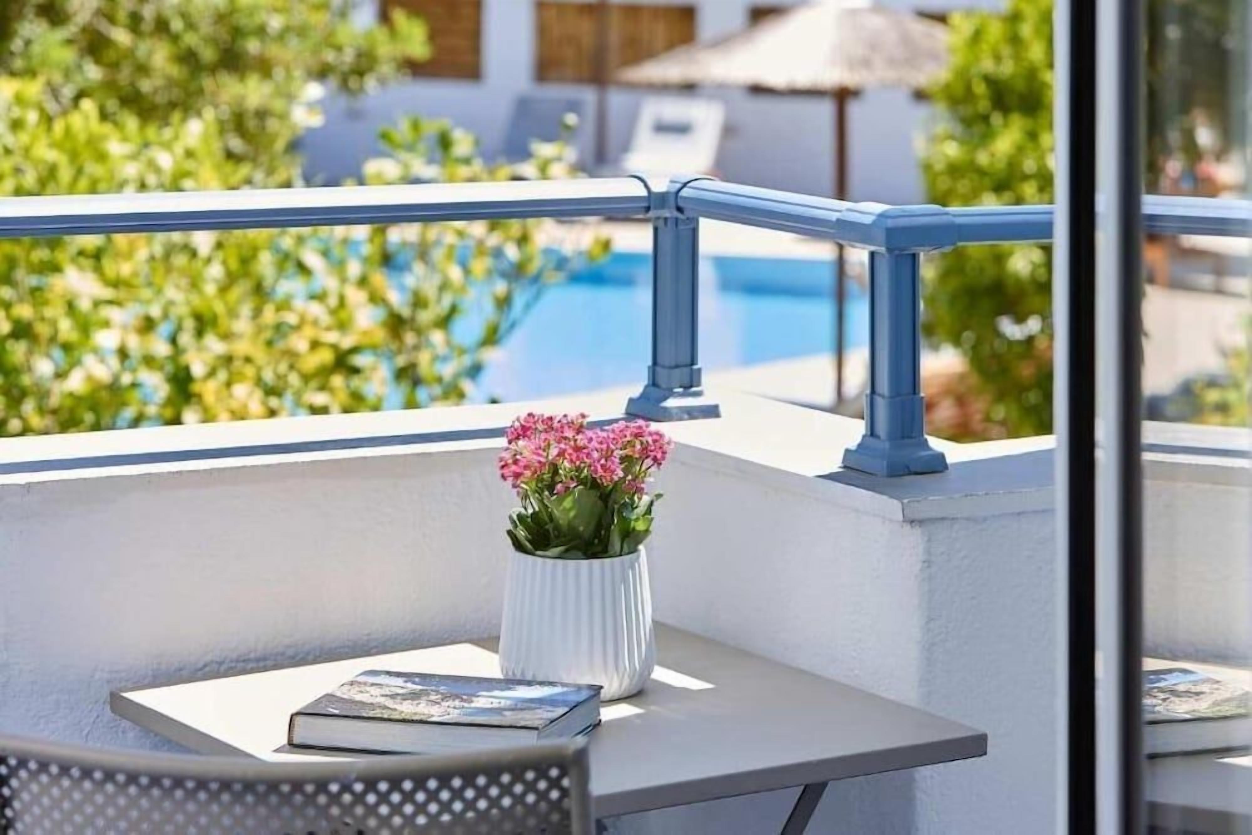 A balcony with a white railing, a white vase with pink flowers, and a book on a table.