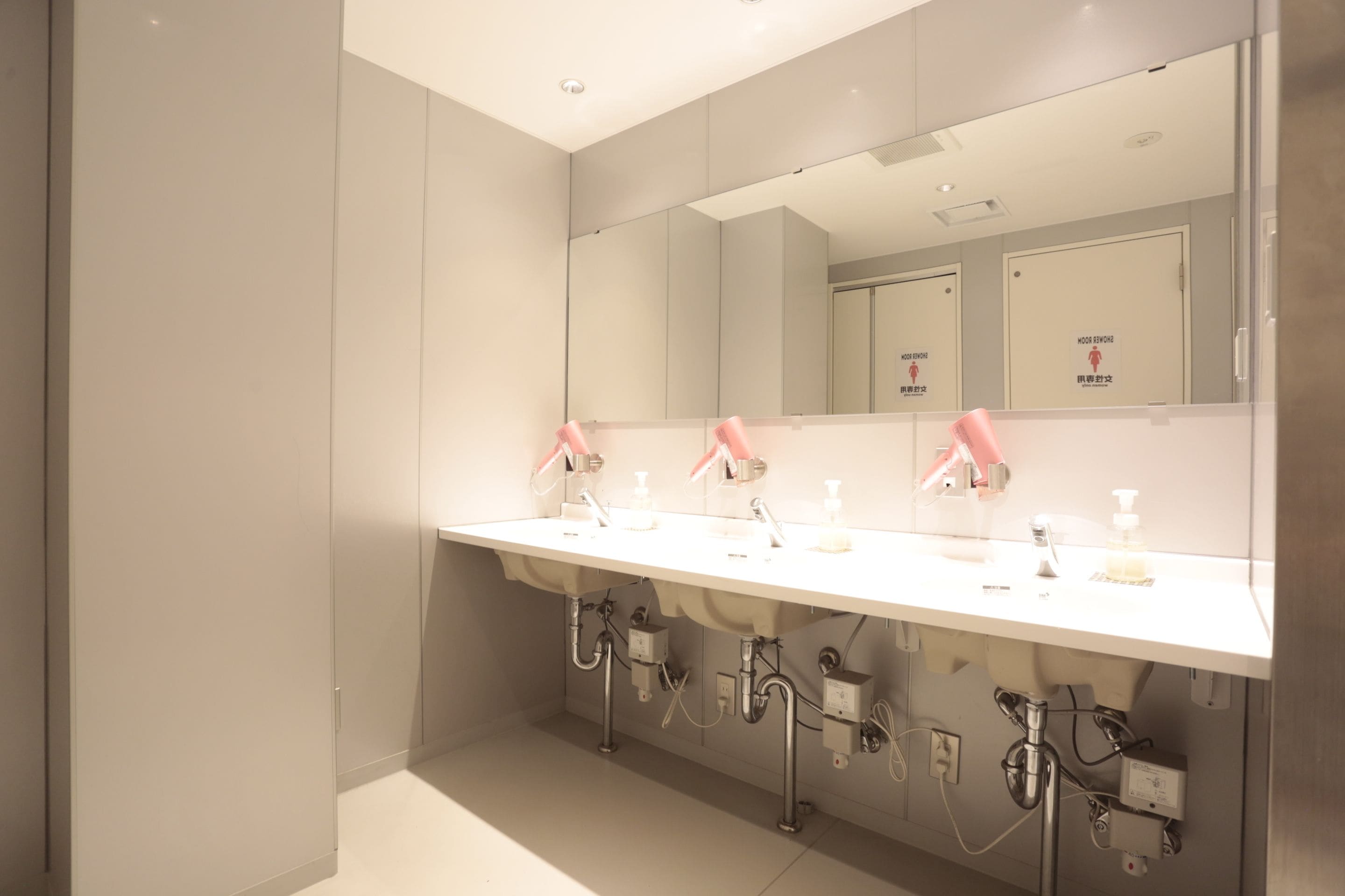 Un baño moderno con un lavamanos blanco, dos grifos rosa y un espejo grande.