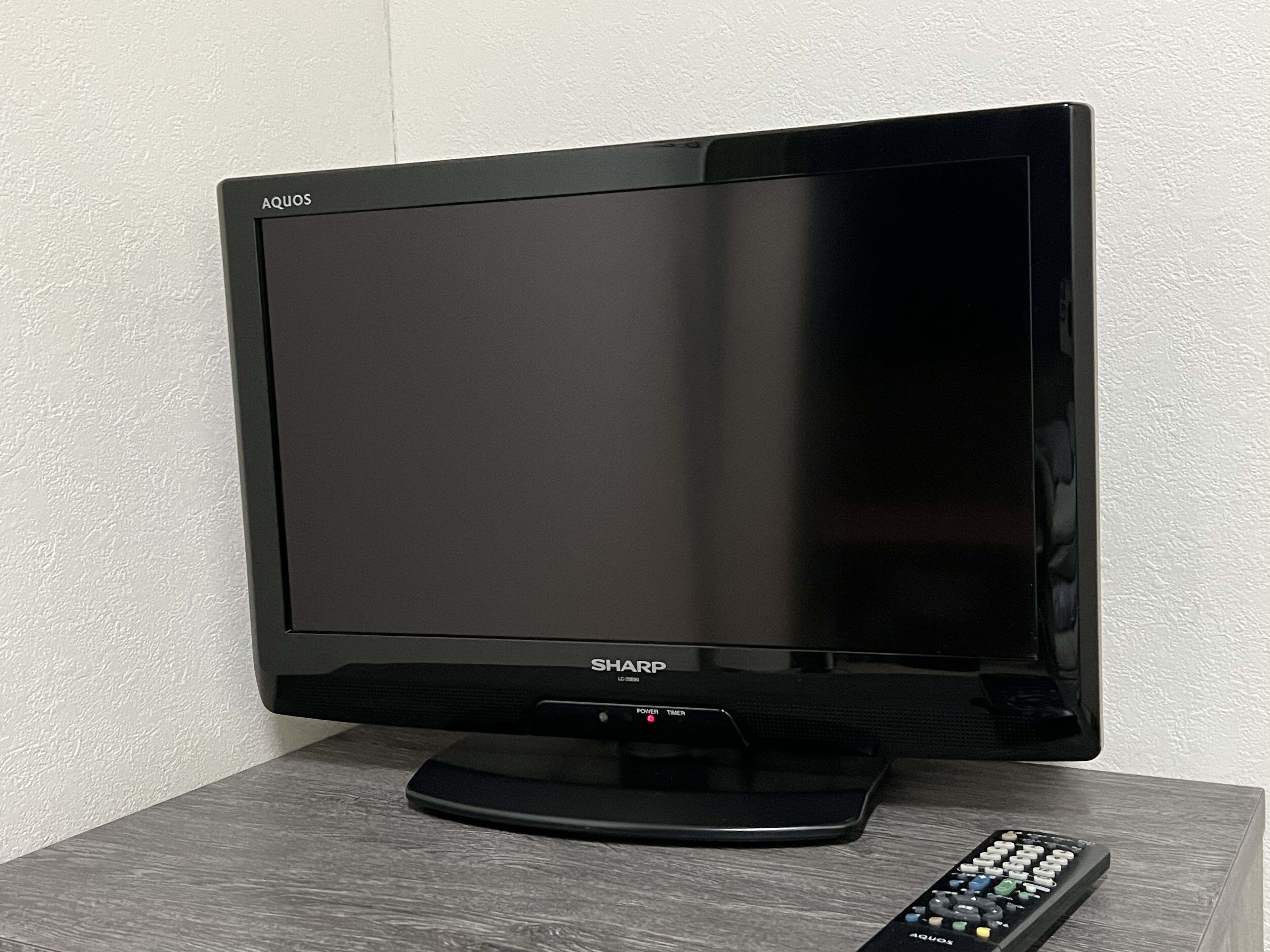 A black Sharp LCD TV on a wooden table against a textured white wall.