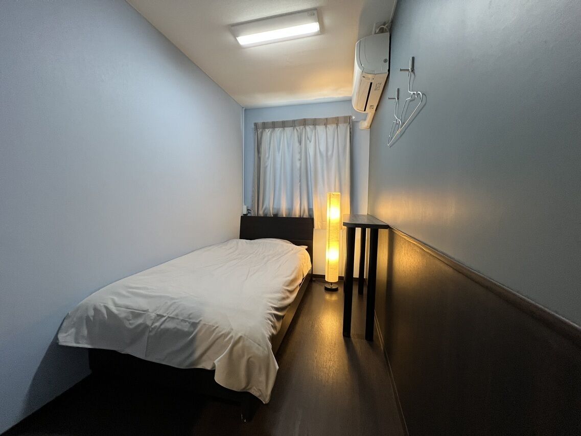Ein Hotelzimmer mit Bett, Nachttisch, Lampe, Klimaanlage und einem Fenster mit Vorhängen.