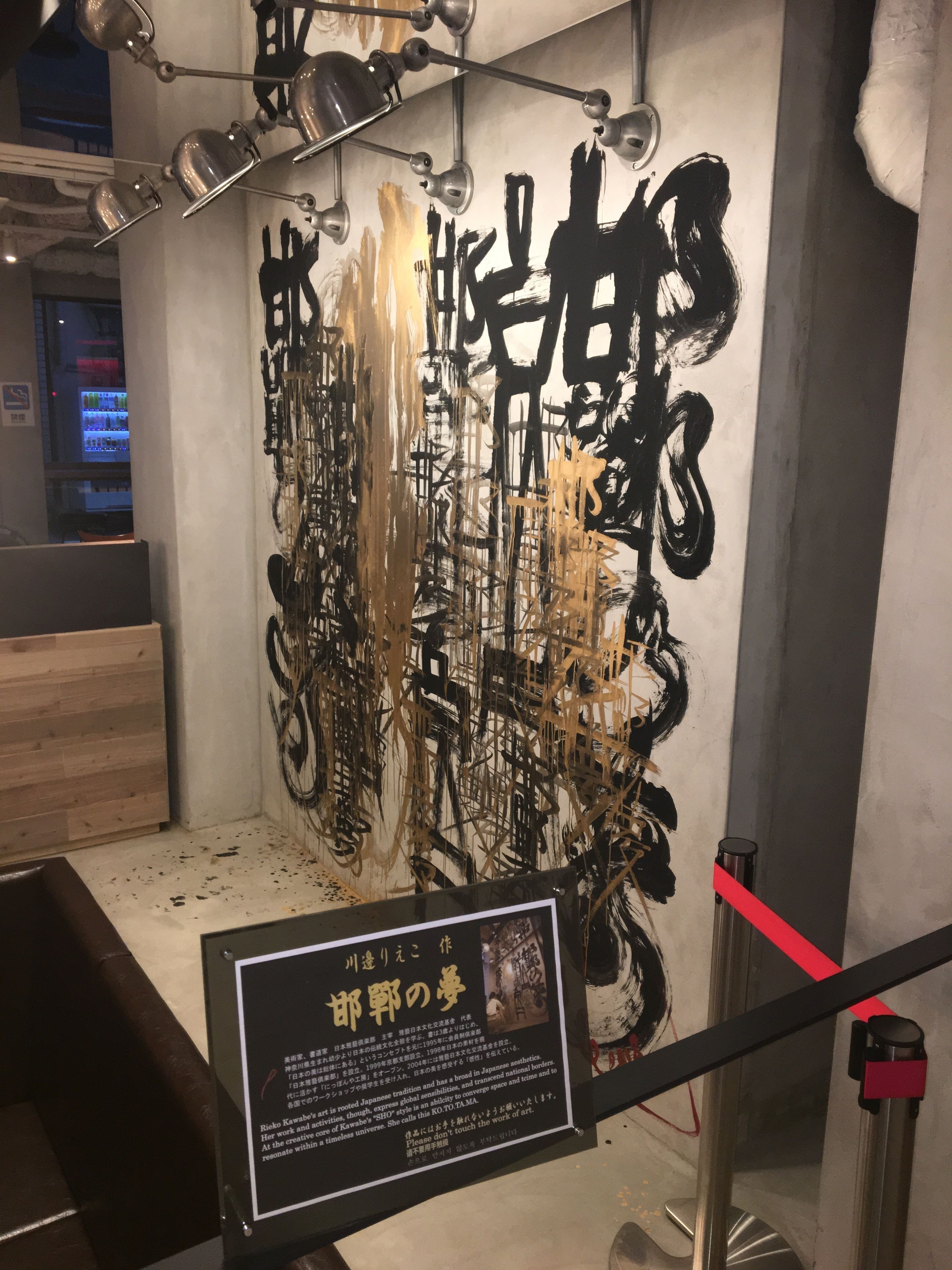 Una pared con arte abstracto y un letrero con texto en japonés.