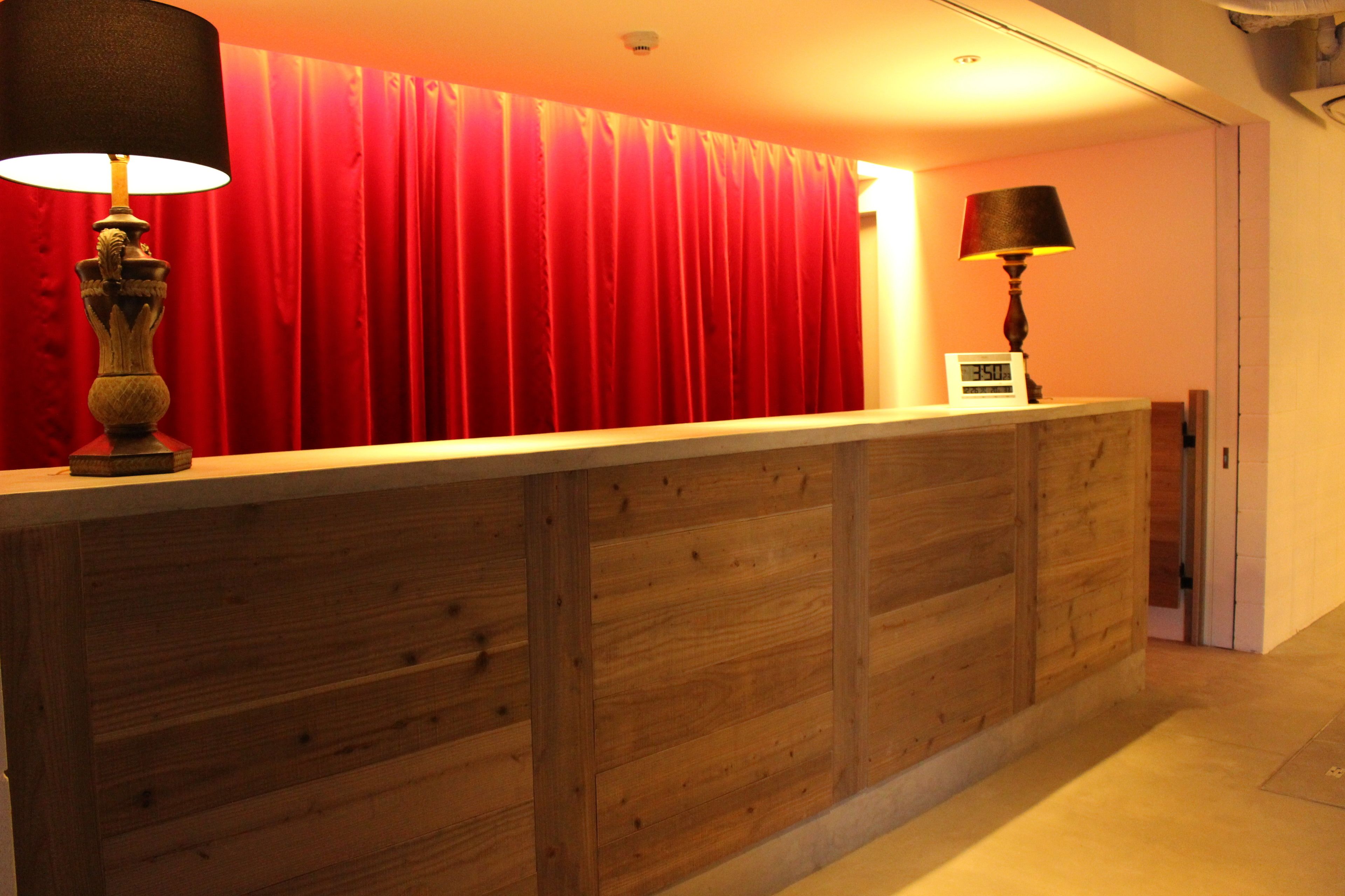 A reception desk with a wooden finish, a red curtain backdrop, and two lamps.