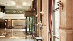 Un vestíbulo amplio con un ascensor moderno, elegantes apliques de pared y un suelo de mármol pulido.