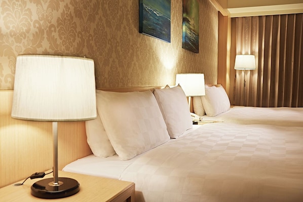 Habitación de hotel con dos camas, cada una con una mesita de noche y lámpara, papel tapiz estampado y un cuadro en la pared.