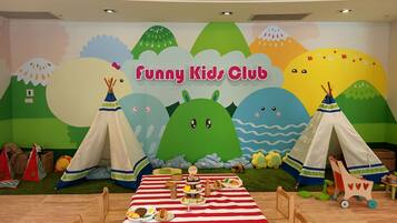 A children's club room with a mural, a table set for a meal, and play tents.