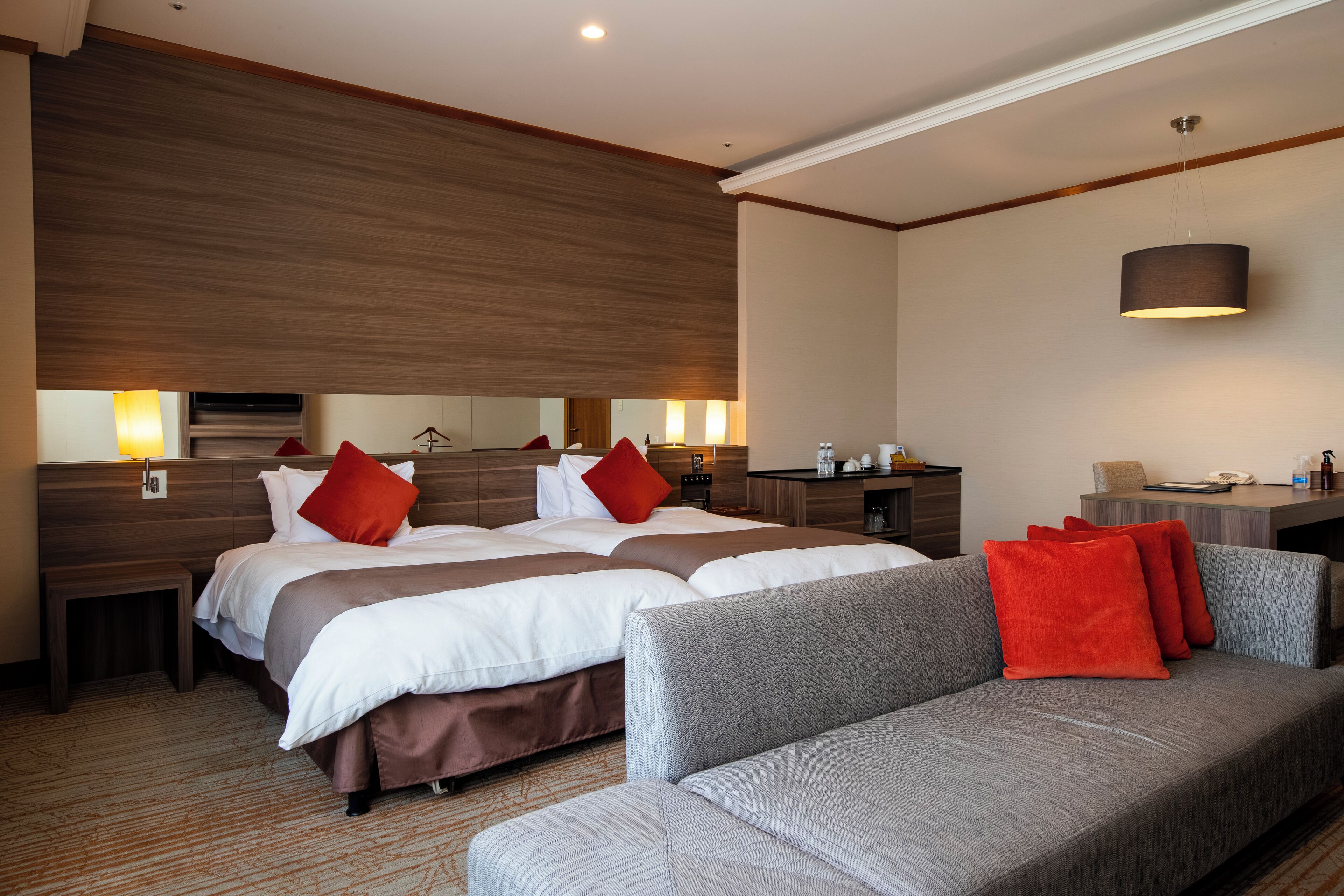 A hotel room with a large bed, a sofa, a desk, and a mirror.