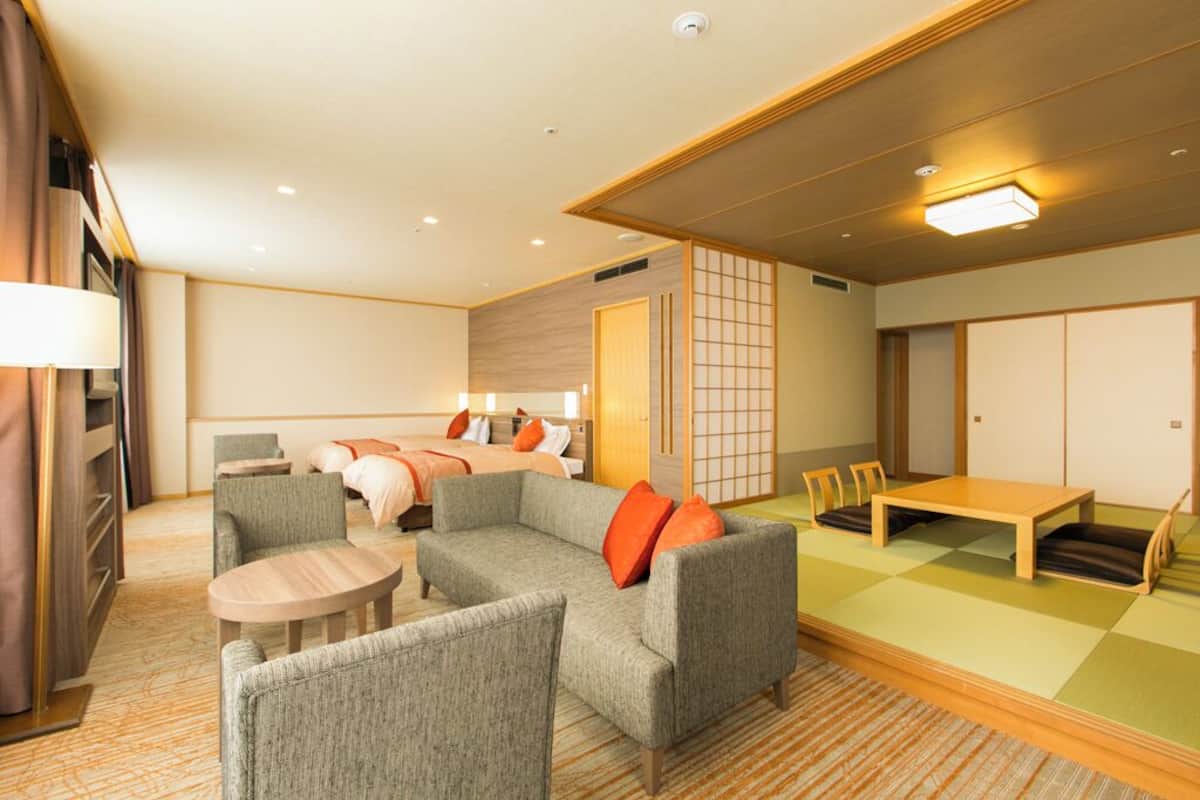 Ein Hotelzimmer mit Sofagarnitur, einem kleinen runden Tisch, einem Bett mit zwei Kissen und einer traditionellen japanischen Schiebetür.