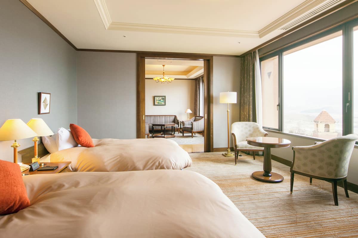 Ein Hotelzimmer mit zwei Betten, einer Sitzecke mit Sofa und Sesseln, einem kleinen Tisch und einem großen Fenster mit Blick.