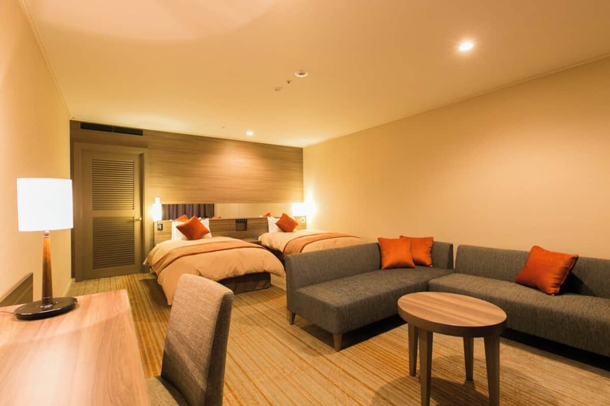 Ein Hotelzimmer mit zwei Betten, einem Schlafsofa, einem kleinen Tisch und einer Lampe.