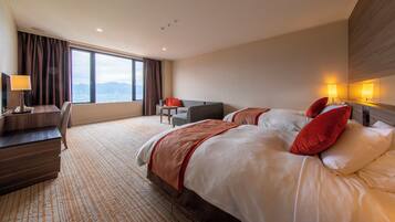 A hotel room with two beds, a desk, a chair, and a view of the mountains.