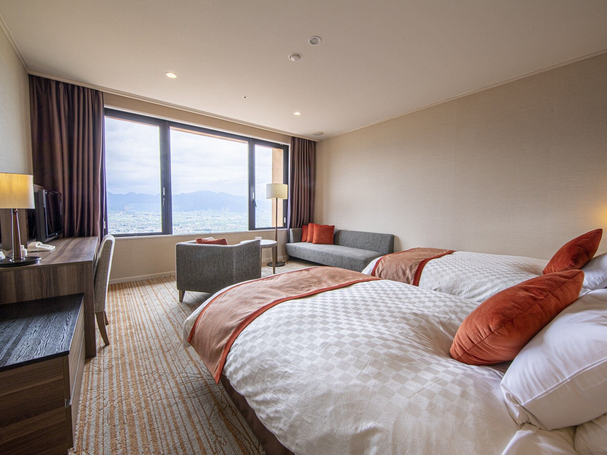 Een hotelkamer met twee bedden, een bureau, een stoel en uitzicht op zee.