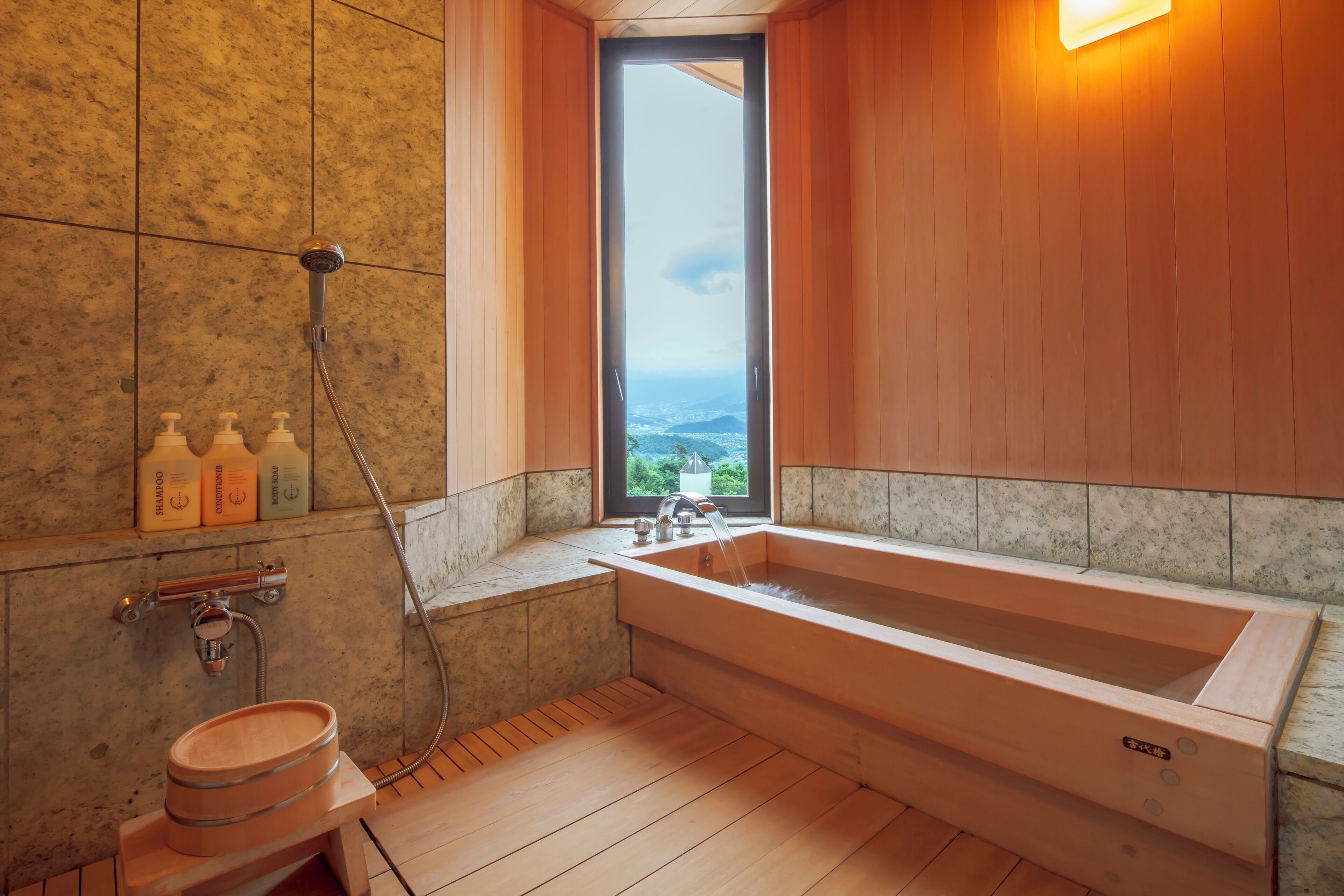 A modern bathroom with a large bathtub, a wooden bench, and a view of the ocean through a window.
