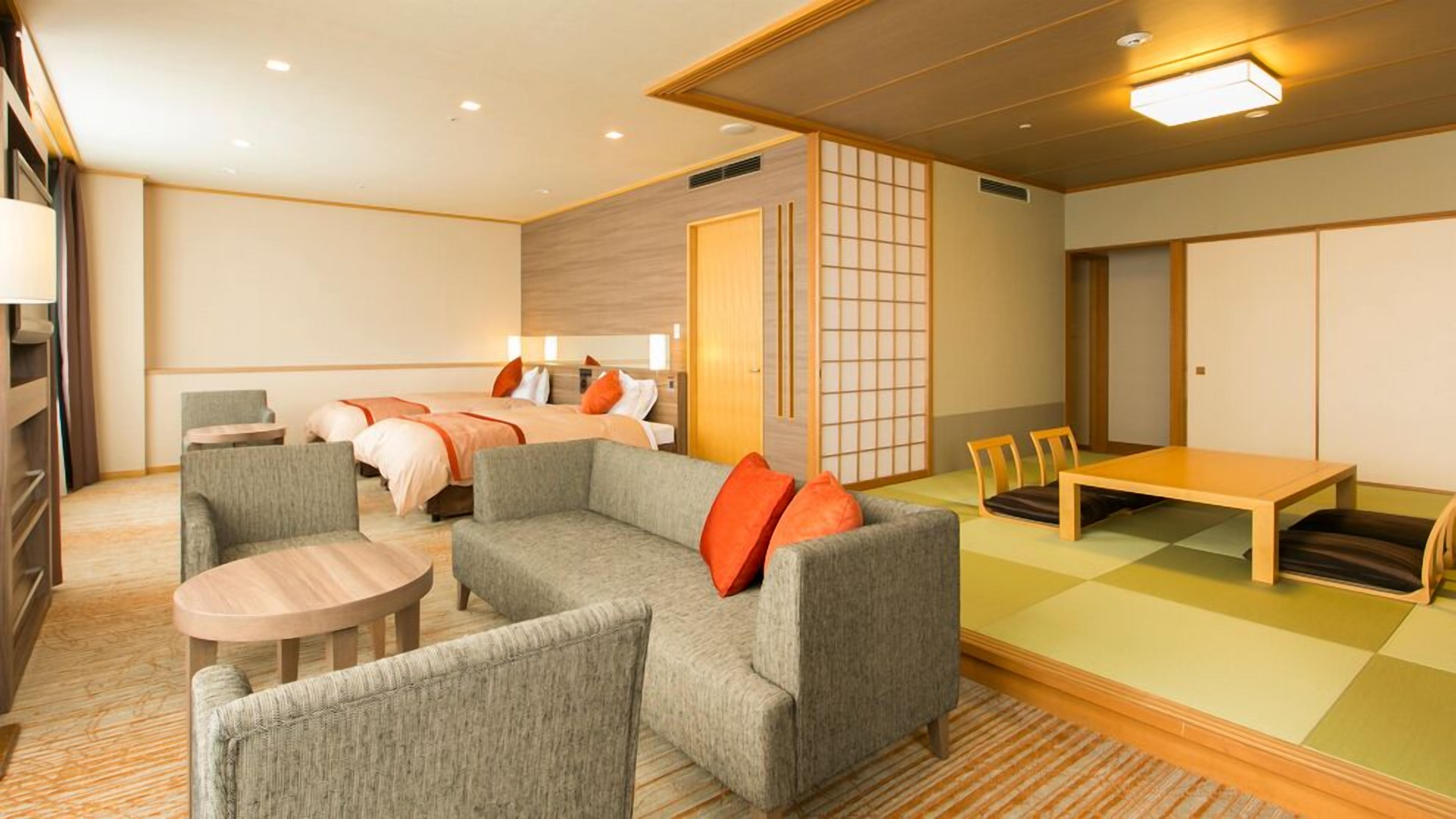 Quarto de hotel com sofá, mesa de jantar, cama com duas almofadas e porta de correr.