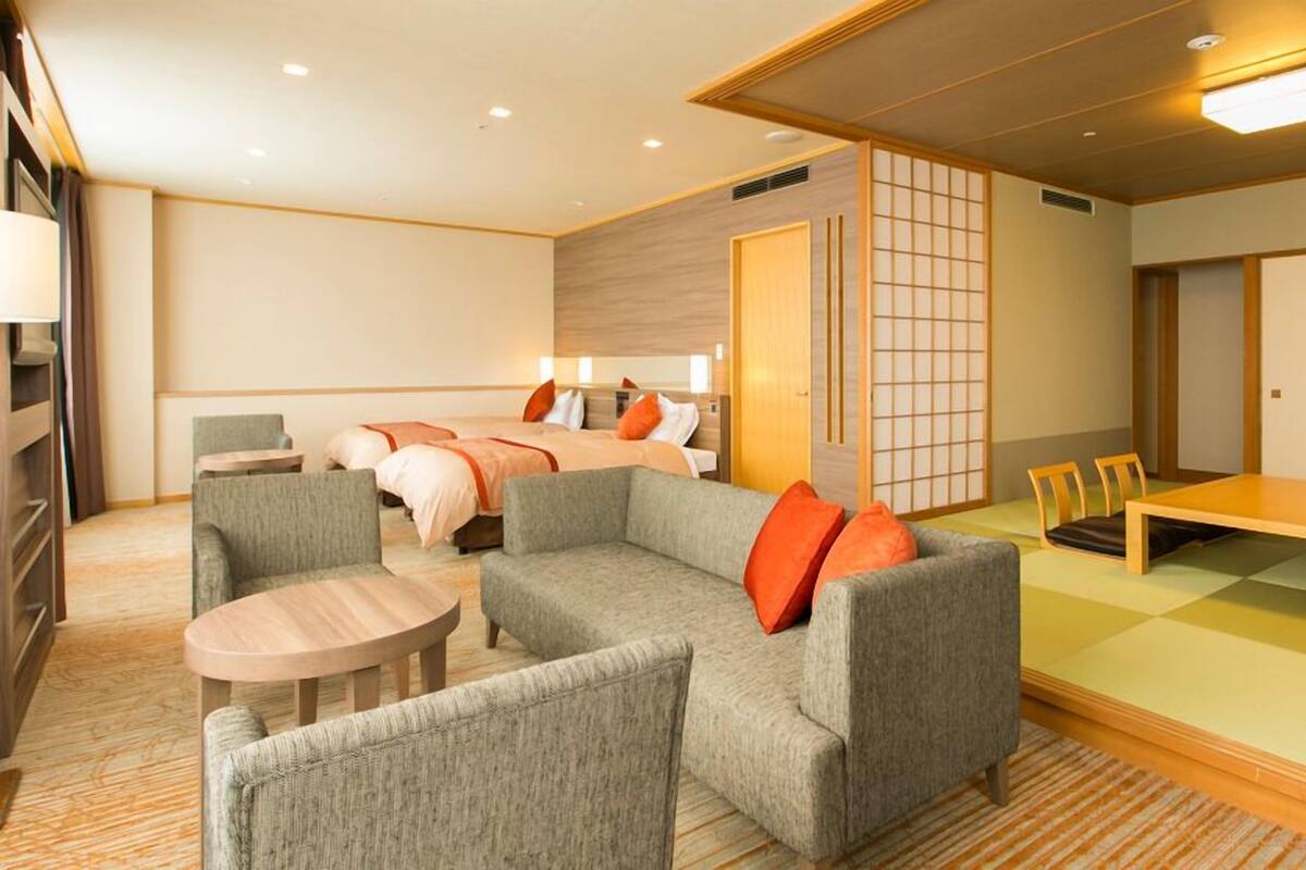 Ein Hotelzimmer mit einer Sofagarnitur, einem Esstisch, einem Bett mit zwei Kissen und einer Schiebetür.