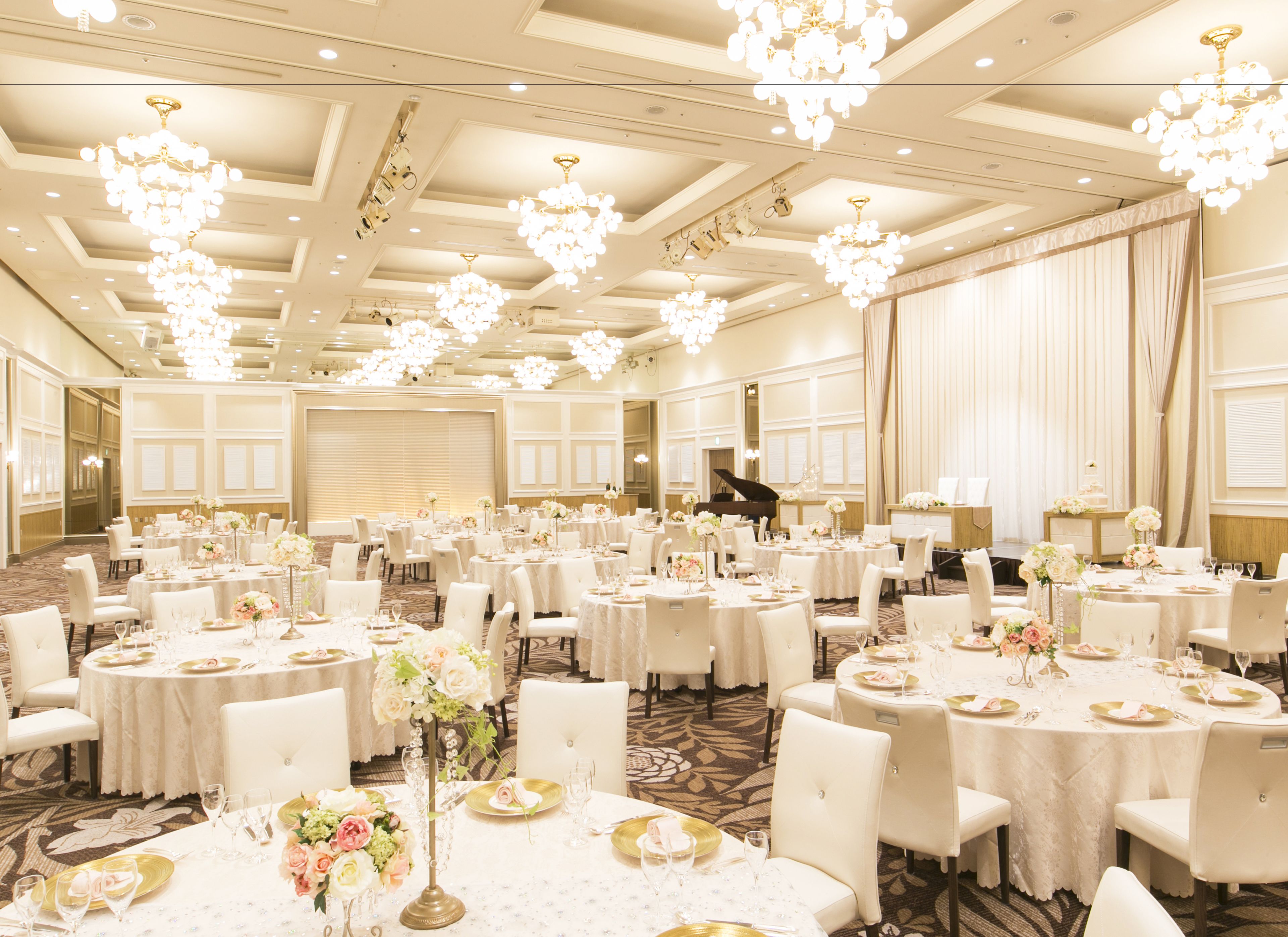 A large banquet hall with round tables, white chairs, and chandeliers.