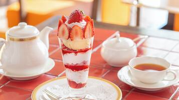 Ein Dessert mit Erdbeeren und Sahne in einem Glas, eine Teekanne, eine Tasse Tee und eine Gabel auf einem Tisch mit roten Fliesen.
