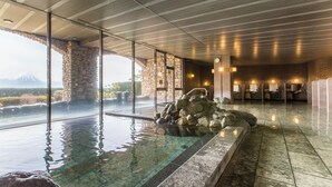 A spa area with a glass-enclosed hot tub, stone pillars, and a view of a mountain. - Fruit Park Fujiya Hotel (Yamanashi)