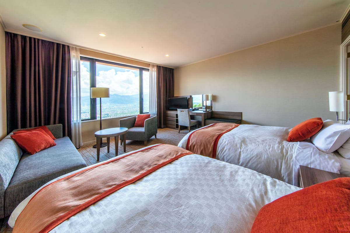 Ein Hotelzimmer mit zwei Betten, einem Schreibtisch, einem Stuhl und einem Fernseher.