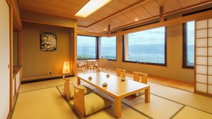 A traditional Japanese room with tatami flooring, a low wooden table with cushions, and large windows offering a view of the sea. - Fruit Park Fujiya Hotel (Yamanashi)