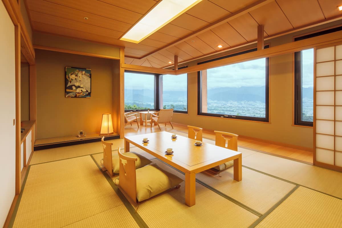 Ein traditioneller japanischer Raum mit Tatami-Böden, einem niedrigen Holztisch mit Kissen und großen Fenstern mit Blick auf das Meer.