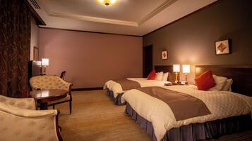 A hotel room with two beds, a chair, a desk, and a lamp.