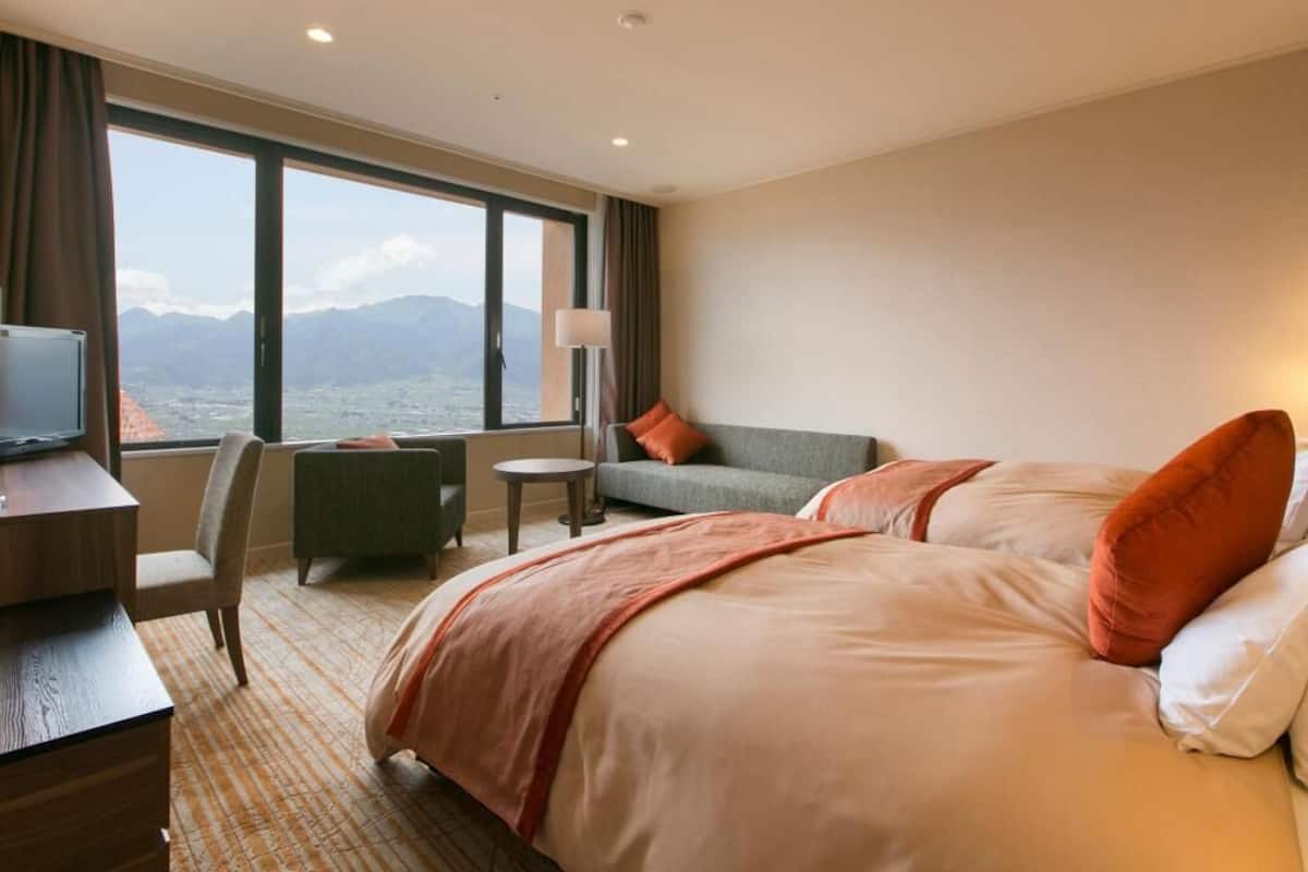 Ein Hotelzimmer mit Bett, Schreibtisch, Stuhl, Sofa und Fernseher.