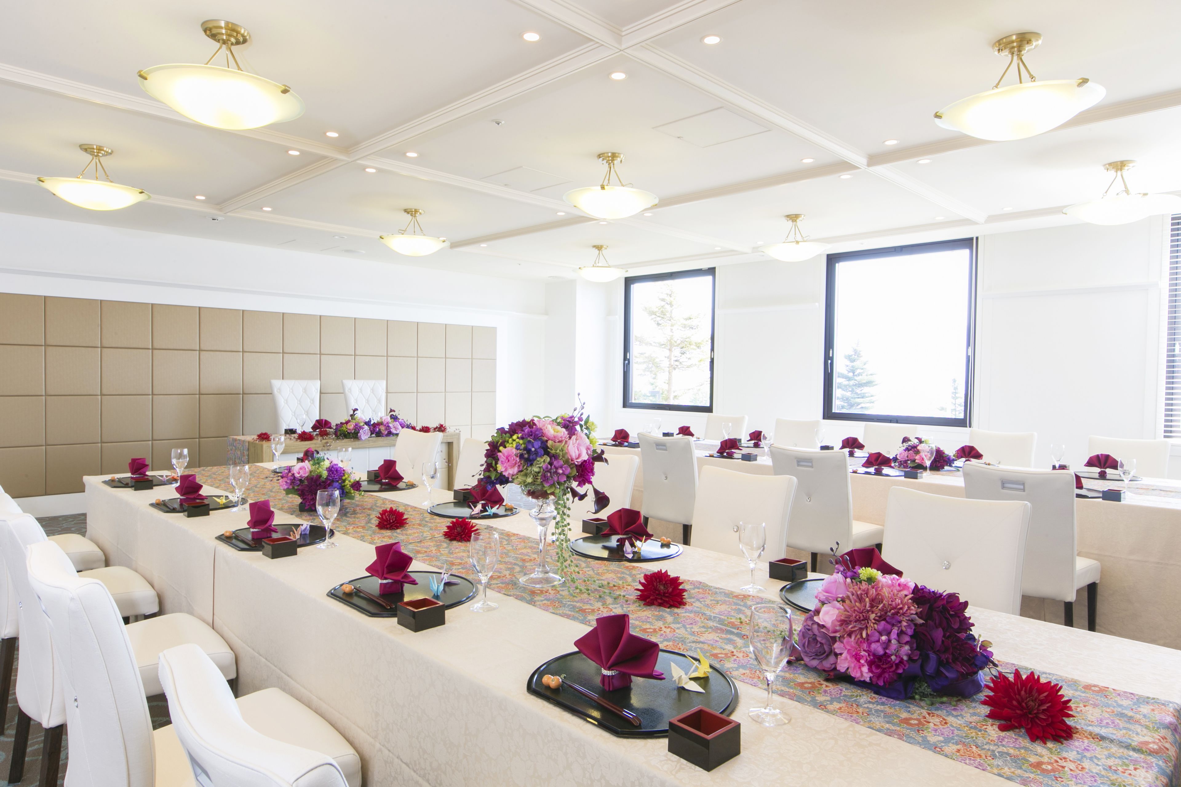 A conference room with a long table set for a meeting, white chairs, and large windows.