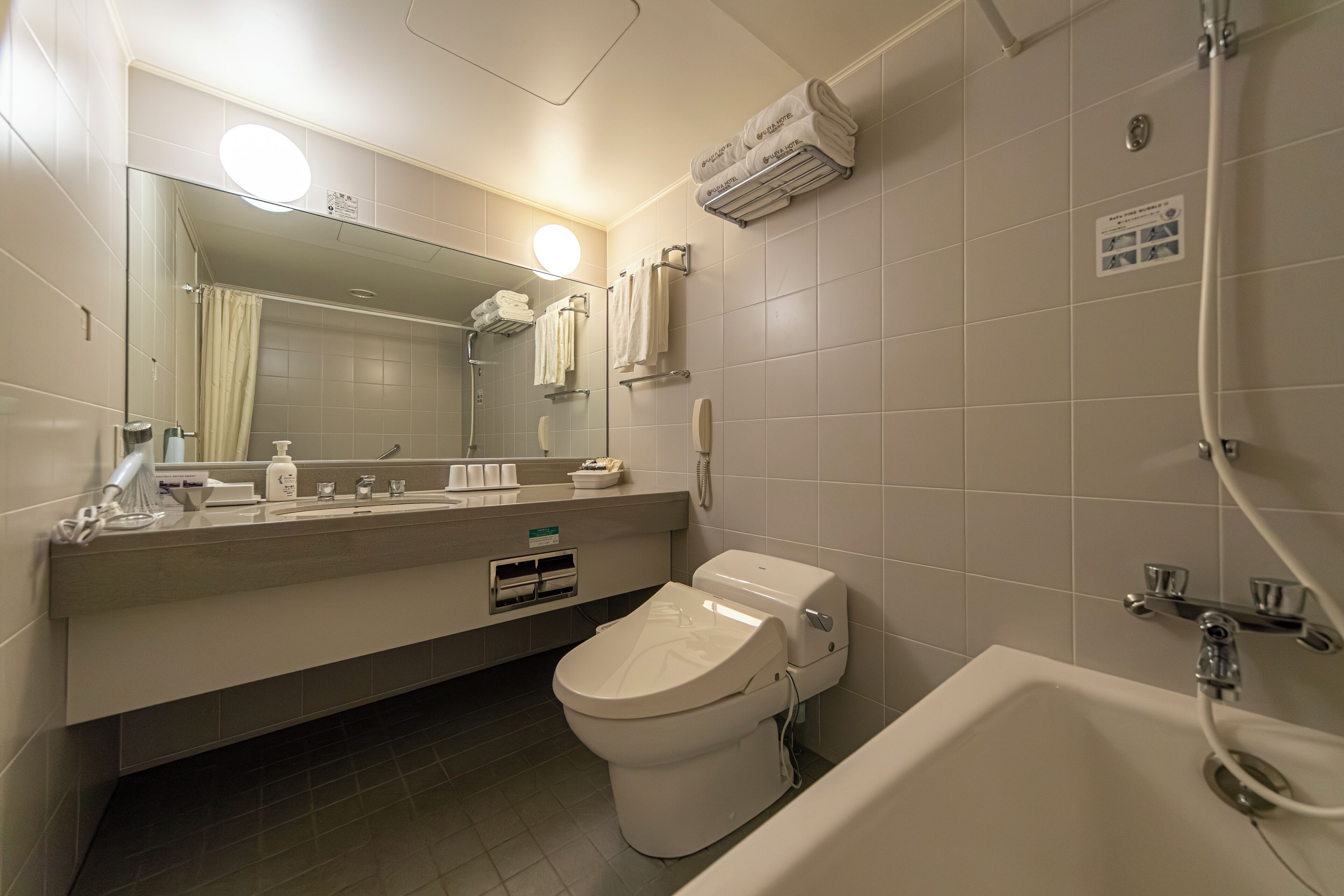 A modern bathroom with a toilet, sink, and bathtub. There is a mirror above the sink, and a towel rack with towels.