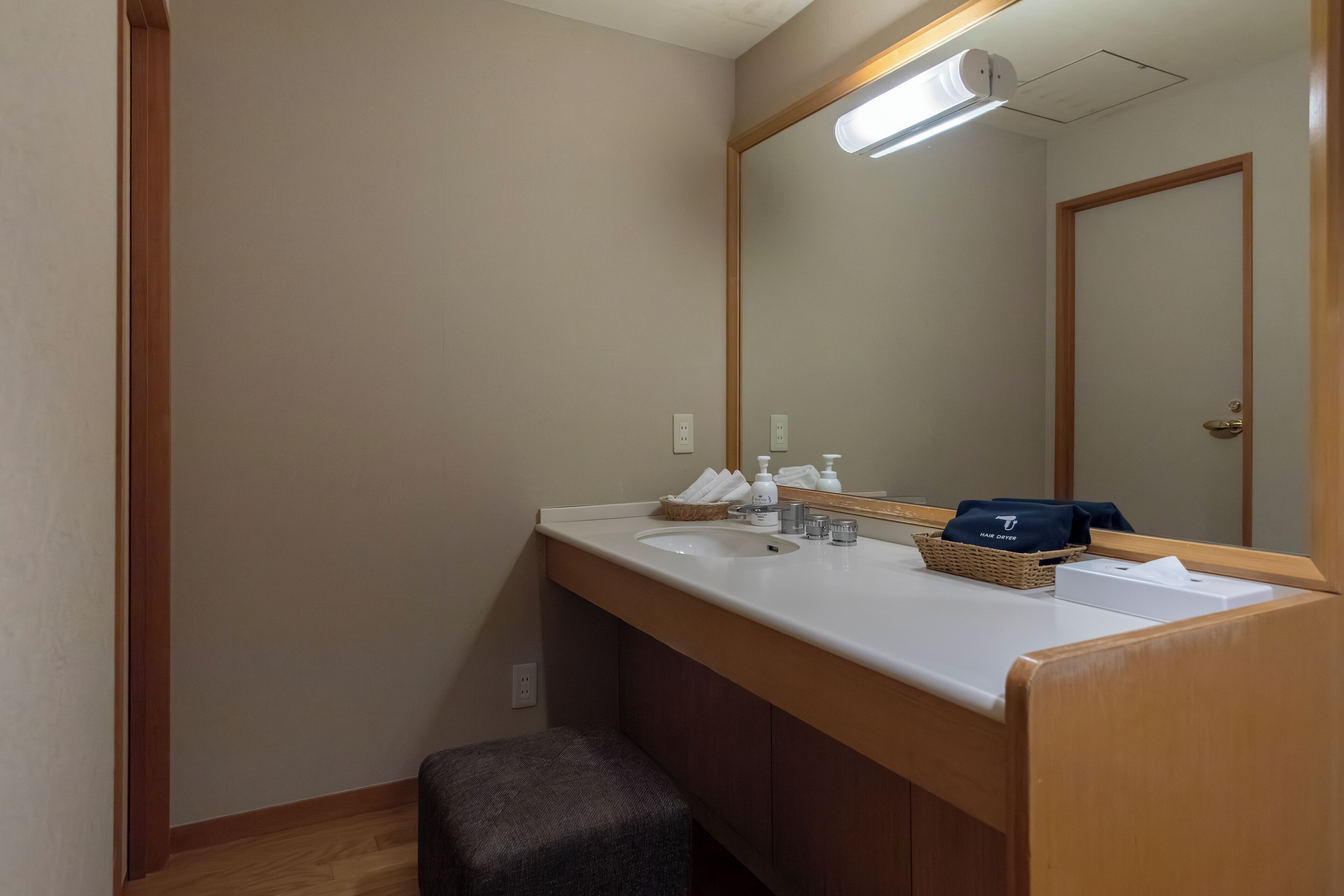 Un baño con lavamanos blanco, un espejo, dispensador de toallas y una cesta con toallas.