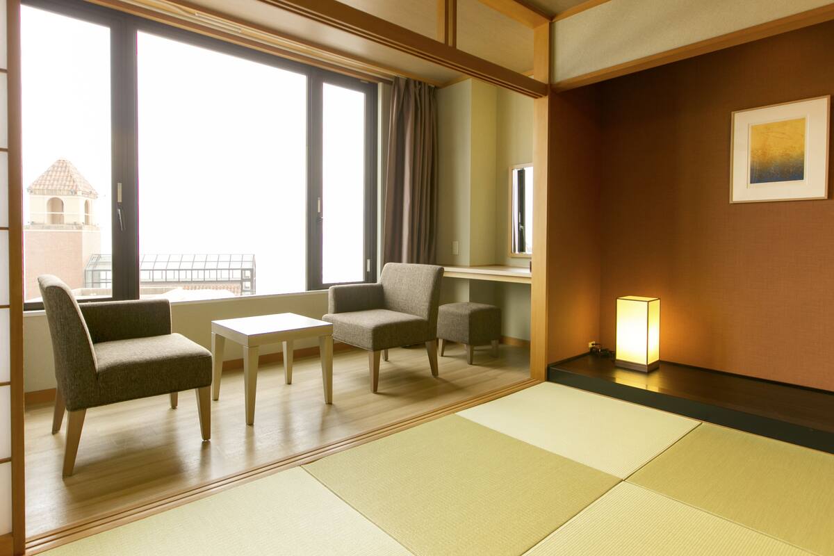 Ein Hotelzimmer mit Tatami-Matten, einer Couch, einem Tisch und einem Stuhl.
