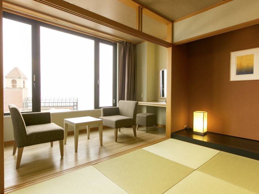 A hotel room with tatami mats, a sofa, a table, and a chair.
