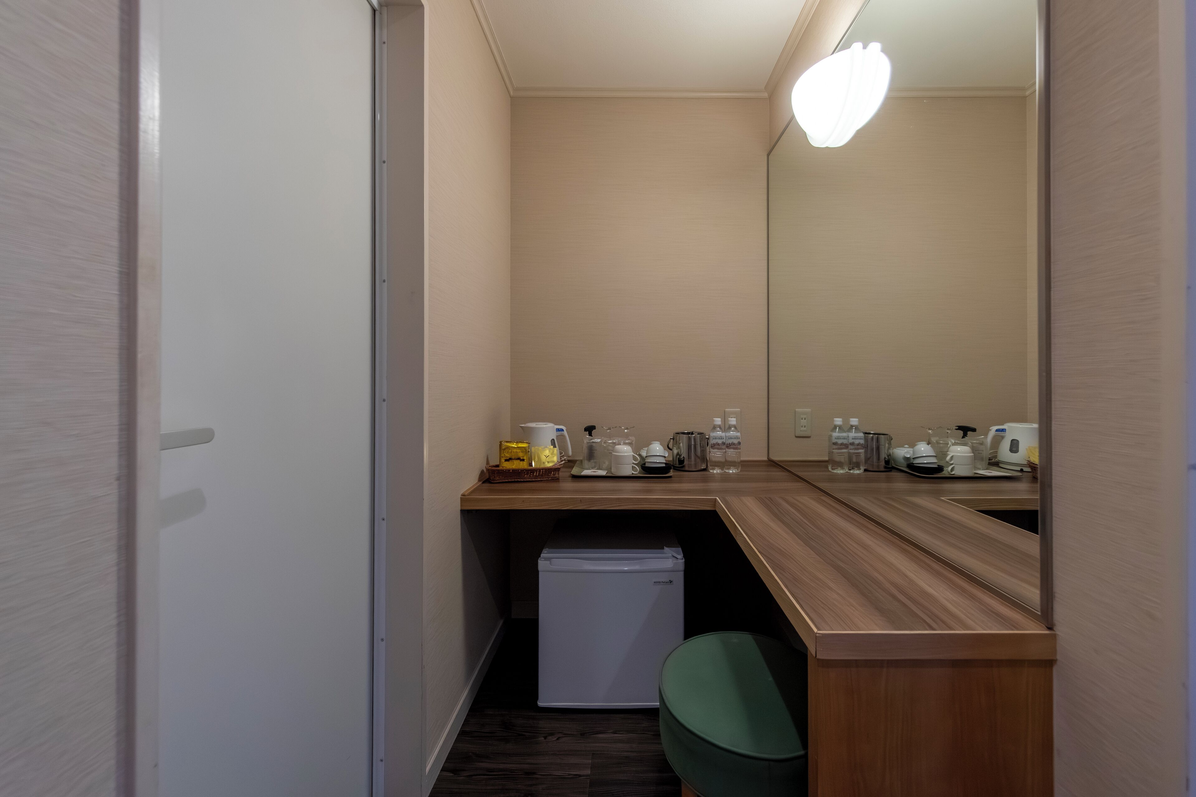 A compact bathroom with a wooden vanity, a mirror, a small refrigerator, and a trash bin.