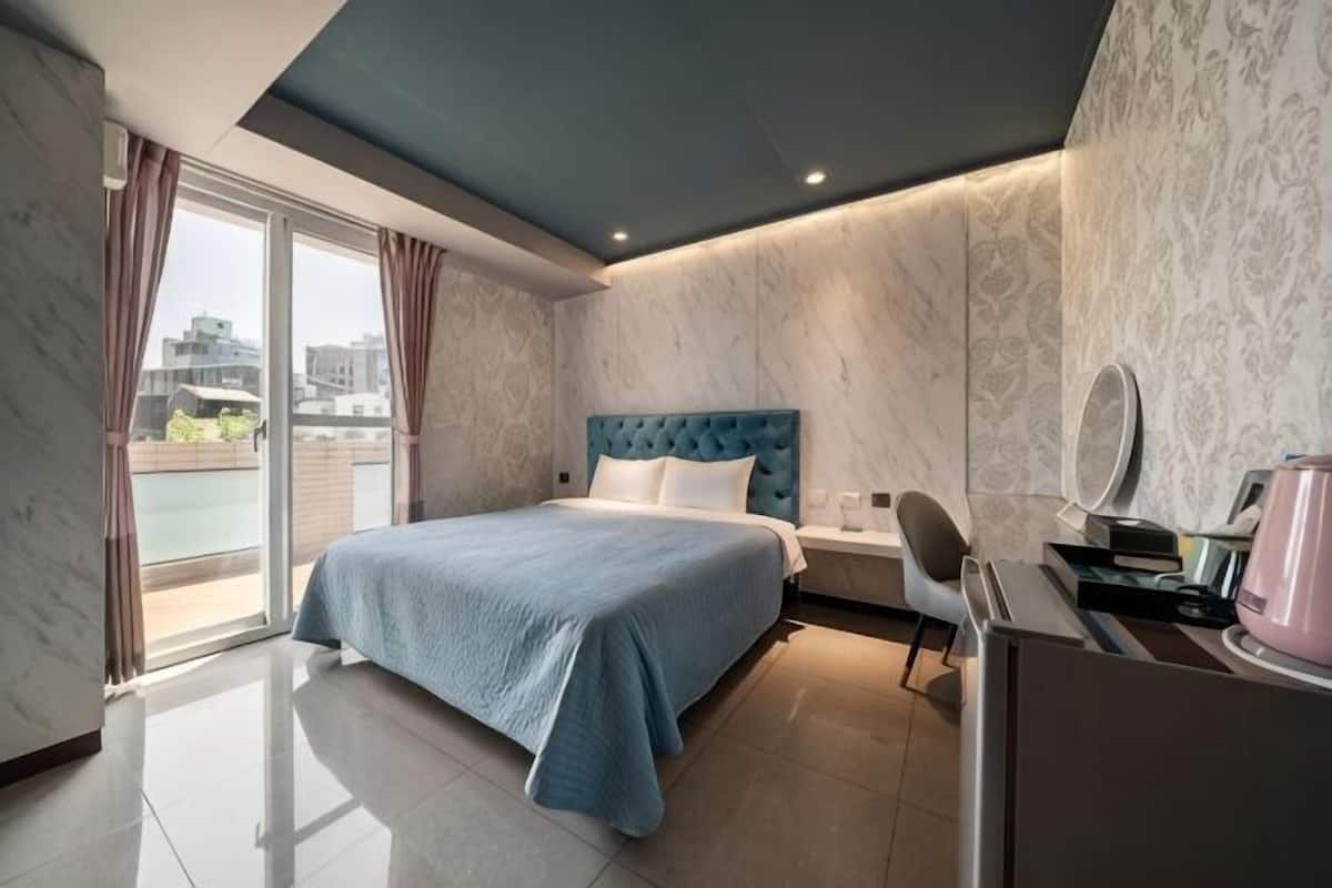 Una habitación de hotel moderna con una cama, un escritorio con espejo y vistas a la ciudad a través de amplios ventanales.
