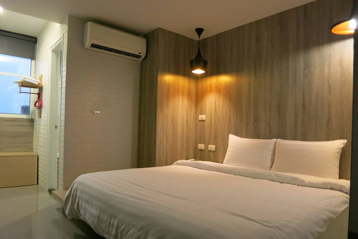 Un dormitorio moderno con una cama grande, paredes de paneles de madera, una lámpara de techo y un equipo de aire acondicionado.