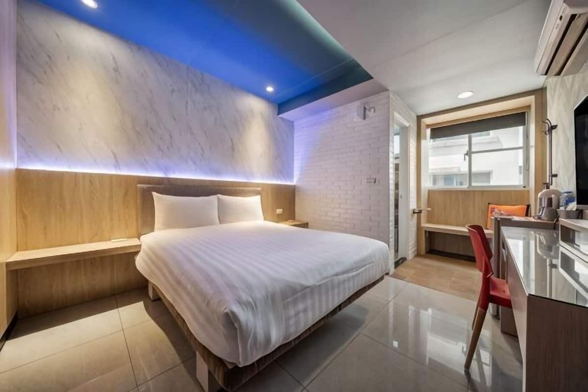 Una habitación de hotel moderna con cama, mesita de noche y una pequeña kitchenette.