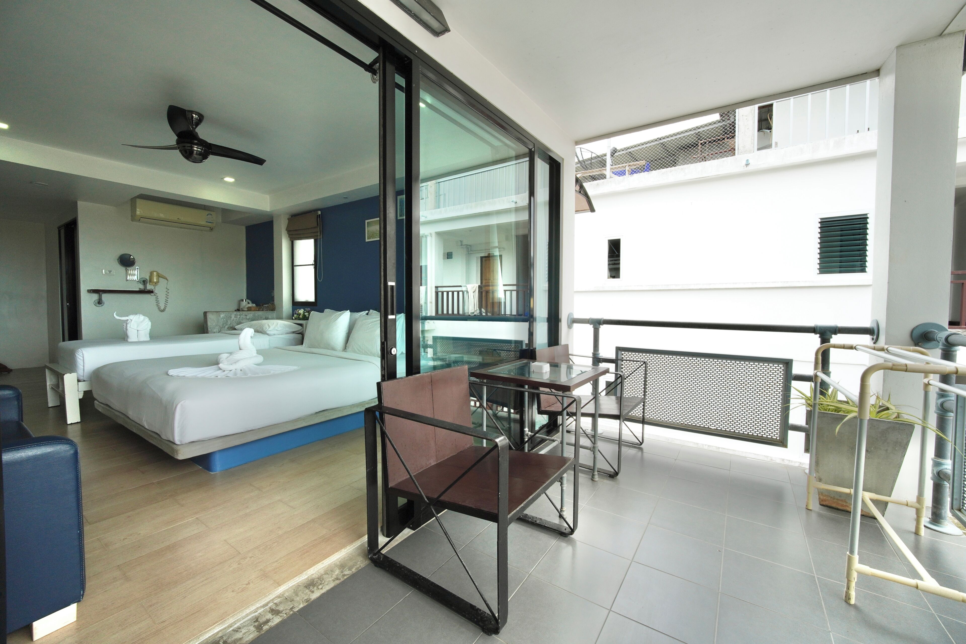 Ein modernes Hotelzimmer mit einem Bett, einem Balkon mit Tisch und Stühlen sowie Blick auf die Außenansicht des Gebäudes.