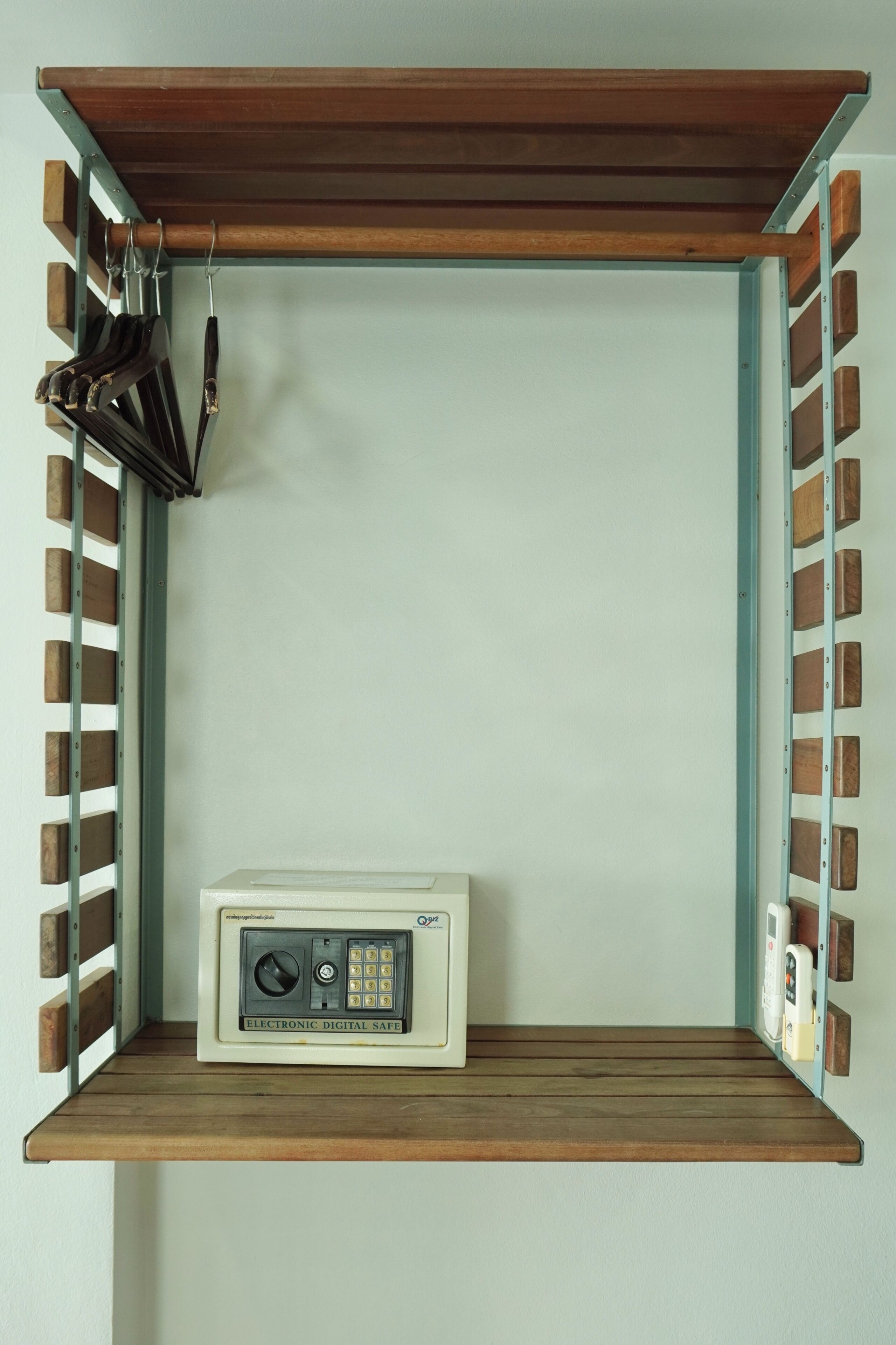 A room with a wooden shelf, a wall-mounted electronic safe, and a set of keys hanging on a metal rack.