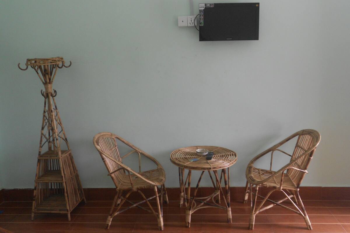 A room with a low table and two wicker chairs, a tall wicker stand, and a wall-mounted TV.