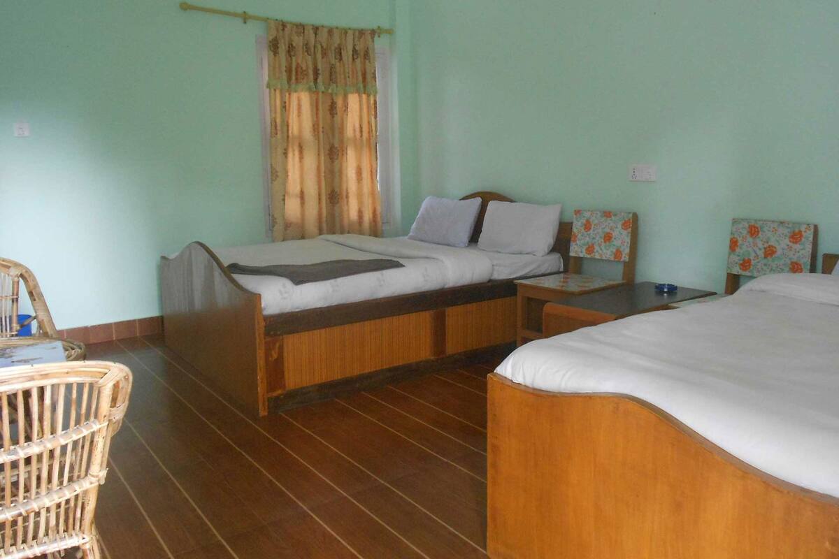 A room with two wooden beds, a small table, a chair, and a window with curtains.