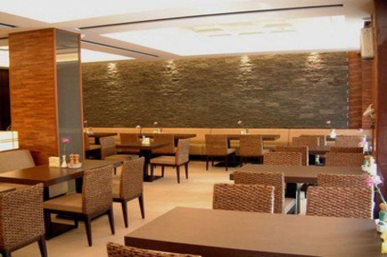 A modern restaurant with wooden tables and chairs, a stone wall feature, and a clean, contemporary design.