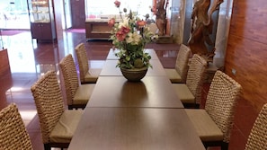A dining area with a long wooden table and woven chairs, a floral centerpiece, and a statue in the background. - Premier Hotel (Tainan)