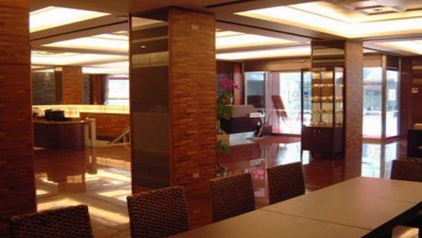 Un hall d’hôtel moderne doté d’un long comptoir d’accueil, d’un espace salon confortable et de grandes fenêtres laissant entrer la lumière naturelle.