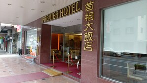 L’entrée du Premier Hotel se distingue par sa façade en verre, son tapis rouge et son enseigne dorée.