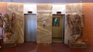 Un ascenseur aux murs de marbre, orné de deux statues représentant des figures ailées, une de chaque côté.