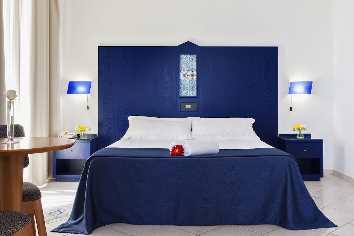 Une chambre d’hôtel avec un grand lit, deux tables de chevet avec des lampes, une petite table ronde et une chaise.