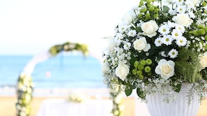 Un vase blanc orné d’un ruban bleu, rempli de fleurs blanches et de verdure, posé sur une table.