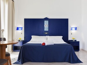 A hotel room with a large bed, two bedside tables with lamps, a small round table, and a chair.