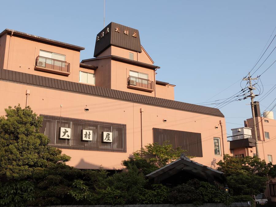 Un edificio moderno con techo plano, múltiples ventanas y un cartel con caracteres japoneses.