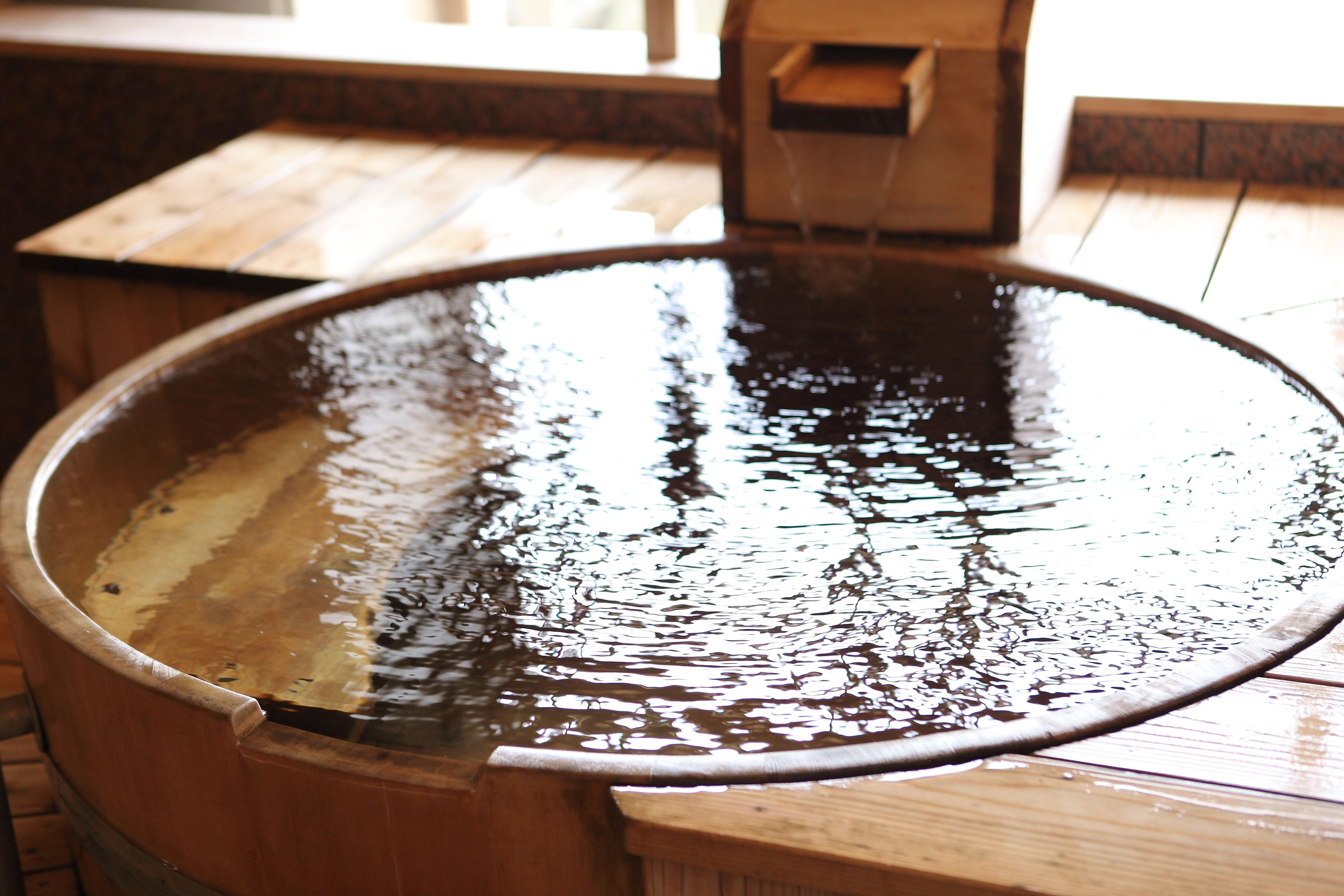 A wooden hot tub with a hose attached, set on a wooden deck.