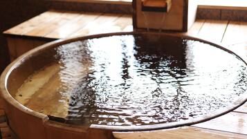 A wooden hot tub with a hose attached, set on a wooden deck.